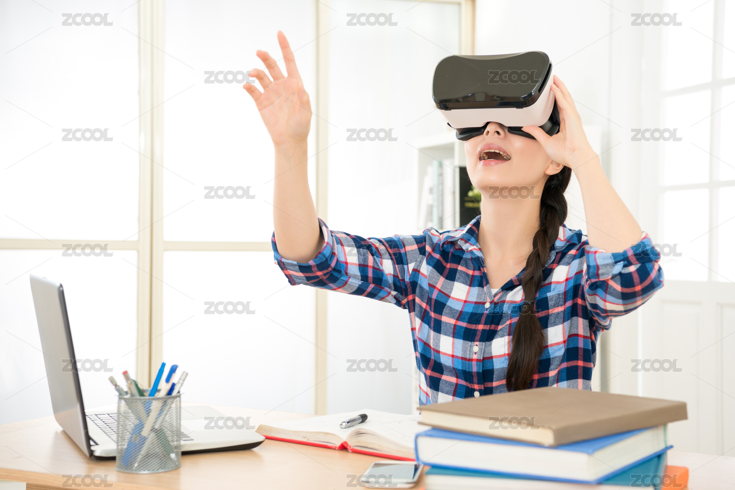 年轻辫子头发的女人穿着虚拟现实眼镜在现代室内设计工作室保持VR护目镜用手势耳机在空气中组织页面。