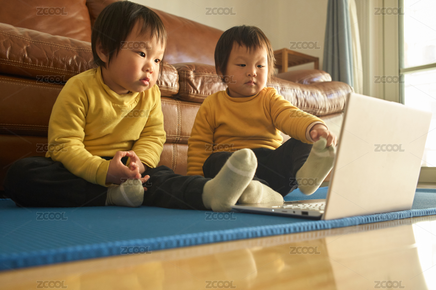 双胞胎婴幼儿坐在瑜伽垫上看笔记本电脑播放