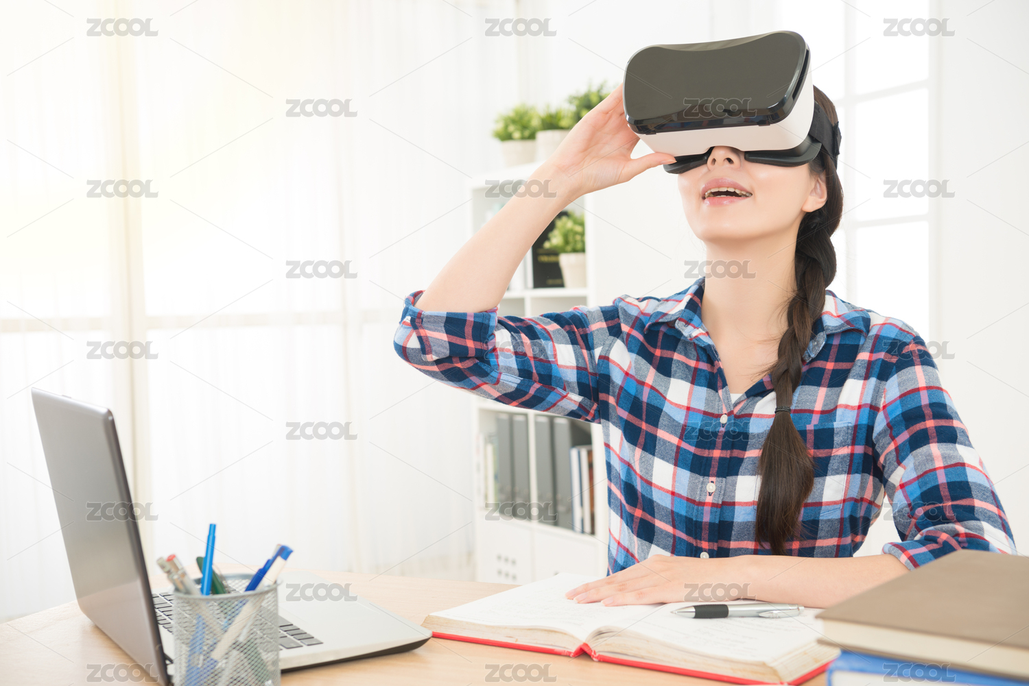 商人坐在办公室，拿着VR体验虚拟现实技术到模拟她的设计项目报告与电脑连接，同时在工作室的办公桌。