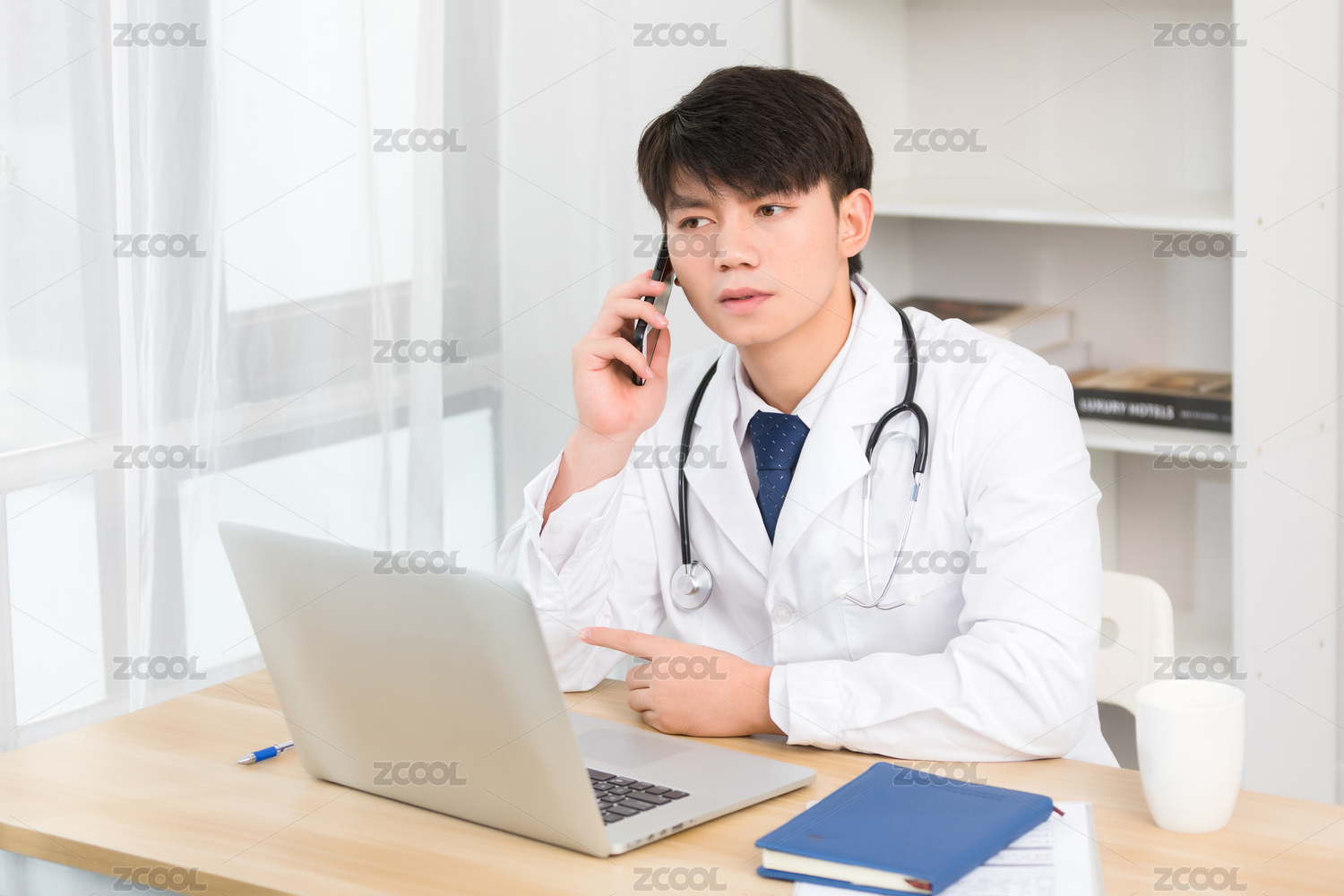 坐在办公室里正在进行电话问诊的亚洲男医生