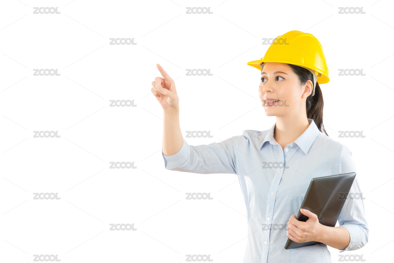 微笑的女人建设者安全头盔衬垫电脑，指着空气COPYSPACE在白墙上按下虚拟图像区域。修复建筑的建设和维护的概念。