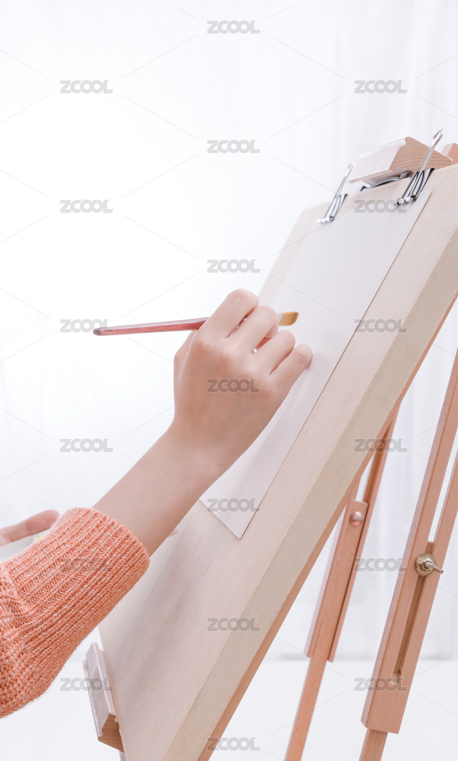 女画家手拿着画笔准备在空白画纸上绘画的特写