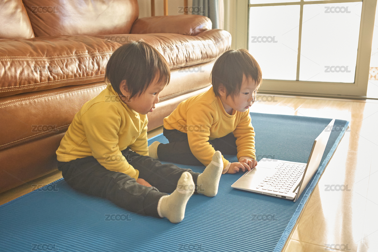 双胞胎婴幼儿坐在瑜伽垫上看笔记本电脑播放