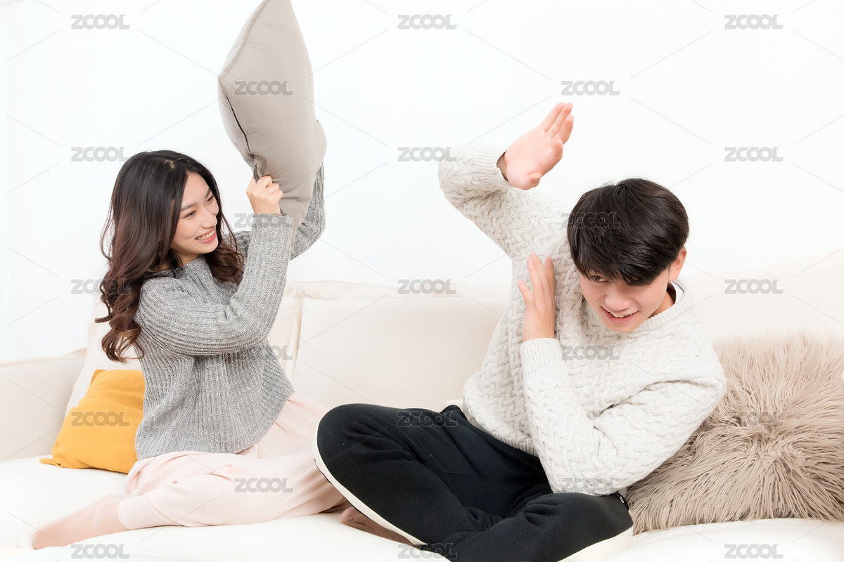 冬天一对高兴的亚洲年轻情侣坐在沙发上，女生用抱枕正在捶打着男生，男生双手抱头不敢反抗（主预览-6039291） - 未分类 - 站酷设计师龙套就是龙套原创素材 - 站酷ZCOOL